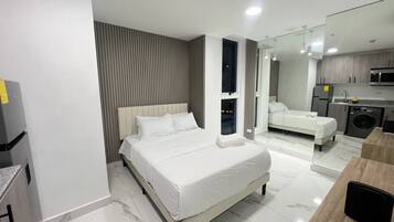 Una habitación de hotel moderna con una cama grande, un armario empotrado, una zona de cocina y un baño con ducha.