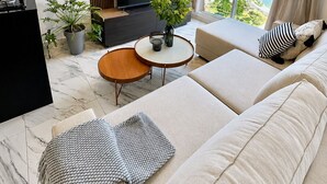 A modern living room with a sofa, a TV, a small table, and a potted plant. - Apartments at The Sands – Ocean View Panama City (Panama City)