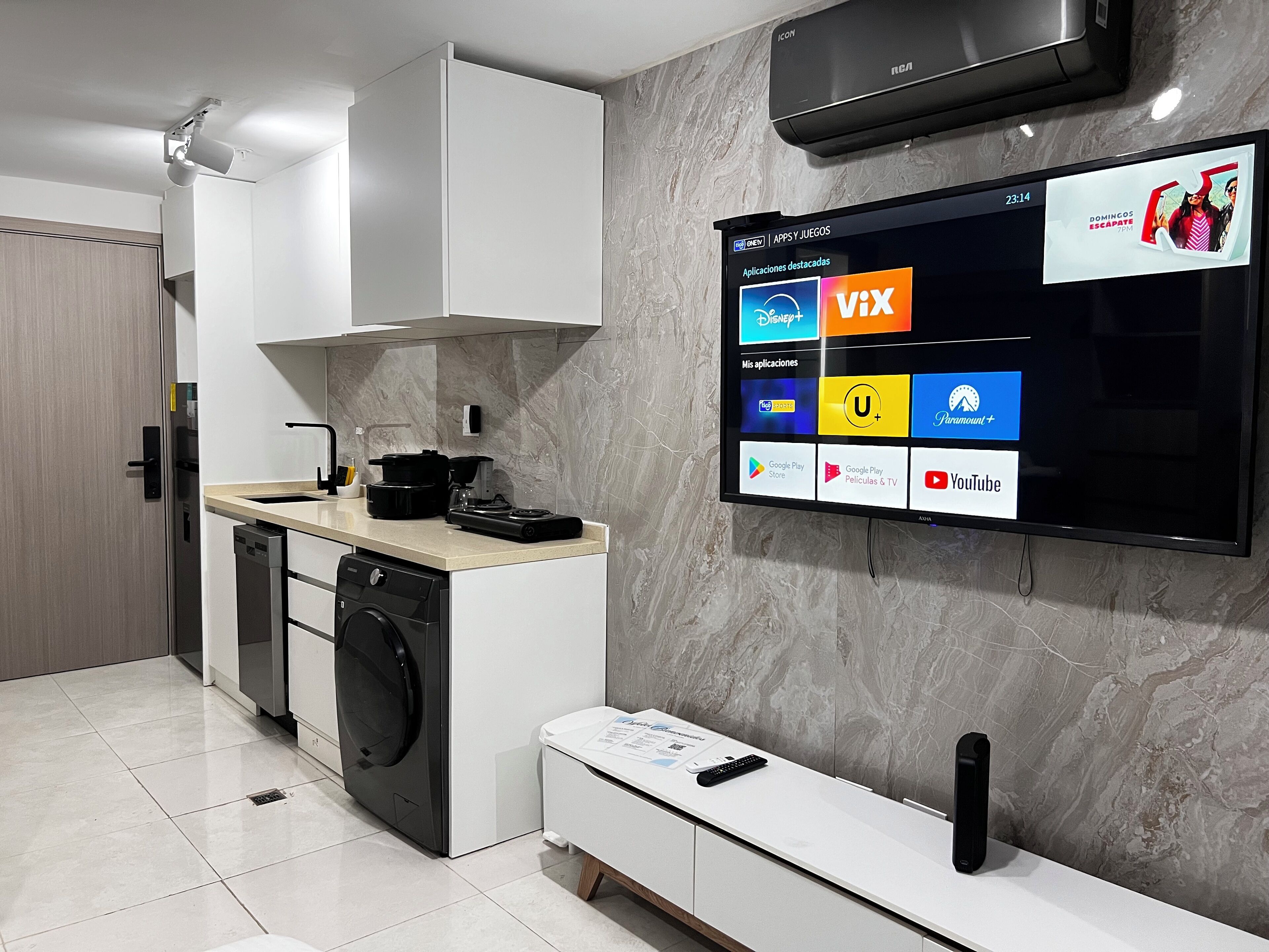 A modern kitchen with a built-in dishwasher, a coffee maker, and a flat-screen TV mounted on the wall displaying various apps.