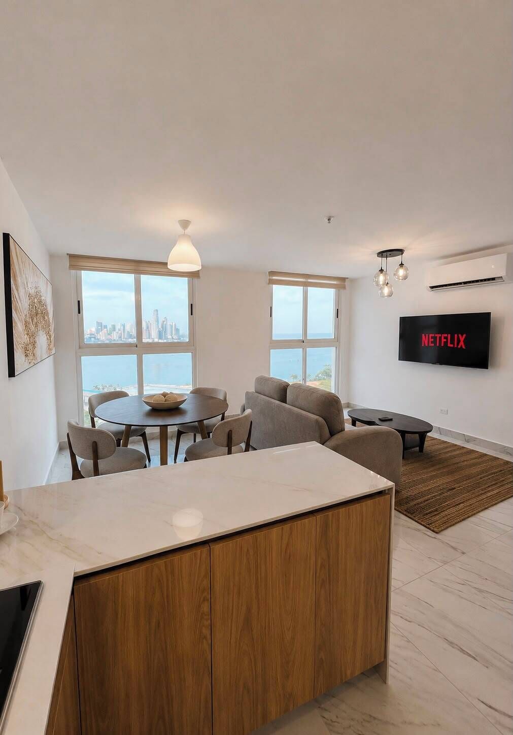 A modern living room with a dining area, large windows, a flat-screen TV, and a city view.