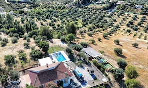 An aerial view of a property with a swimming pool, a tennis court, and a house with a red-tiled roof.