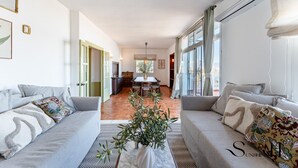 Ein großzügiger Wohnbereich mit zwei grauen Sofas, einem Esstisch und einer Küche im Hintergrund.