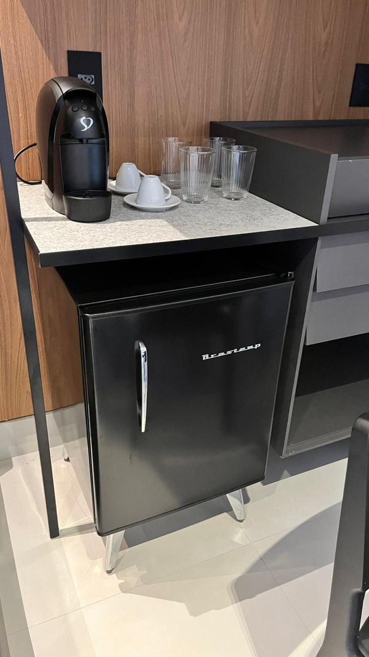 Un petit coin cuisine comprenant une machine à café, quelques tasses et des verres posés sur un plan de travail.