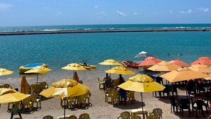 A beach with yellow umbrellas and chairs, a clear blue sky, and the ocean in the background. - PORTO 2 LIFE RESORT - MARÉ ALTA (Ipojuca)