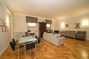 A living room with a sofa, a dining table with chairs, a TV, and a radiator.