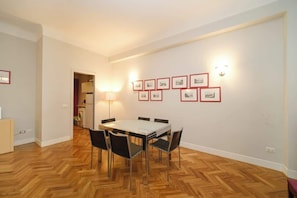A dining area with a table and chairs, a wall-mounted light, and framed pictures.