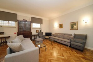 Ein Wohnzimmer mit Sofa, Sessel, Fernseher und Holzboden im Fischgrätmuster.
