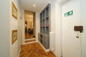 A hallway with a wooden floor, a white door with an emergency exit sign, and a grey cabinet with pink items.