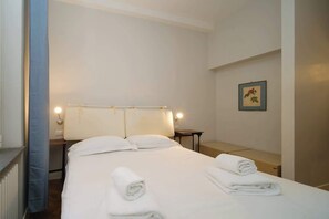 A hotel room with a bed, two bedside tables, a nightstand, a lamp, and a framed picture on the wall.