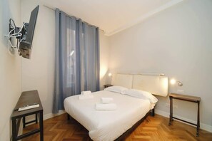A hotel room with a bed, bedside tables, a TV mounted on the wall, and a curtain.