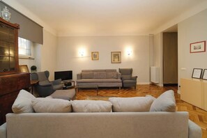 A living room with a sofa, armchairs, a coffee table, a television, and wall-mounted lights.