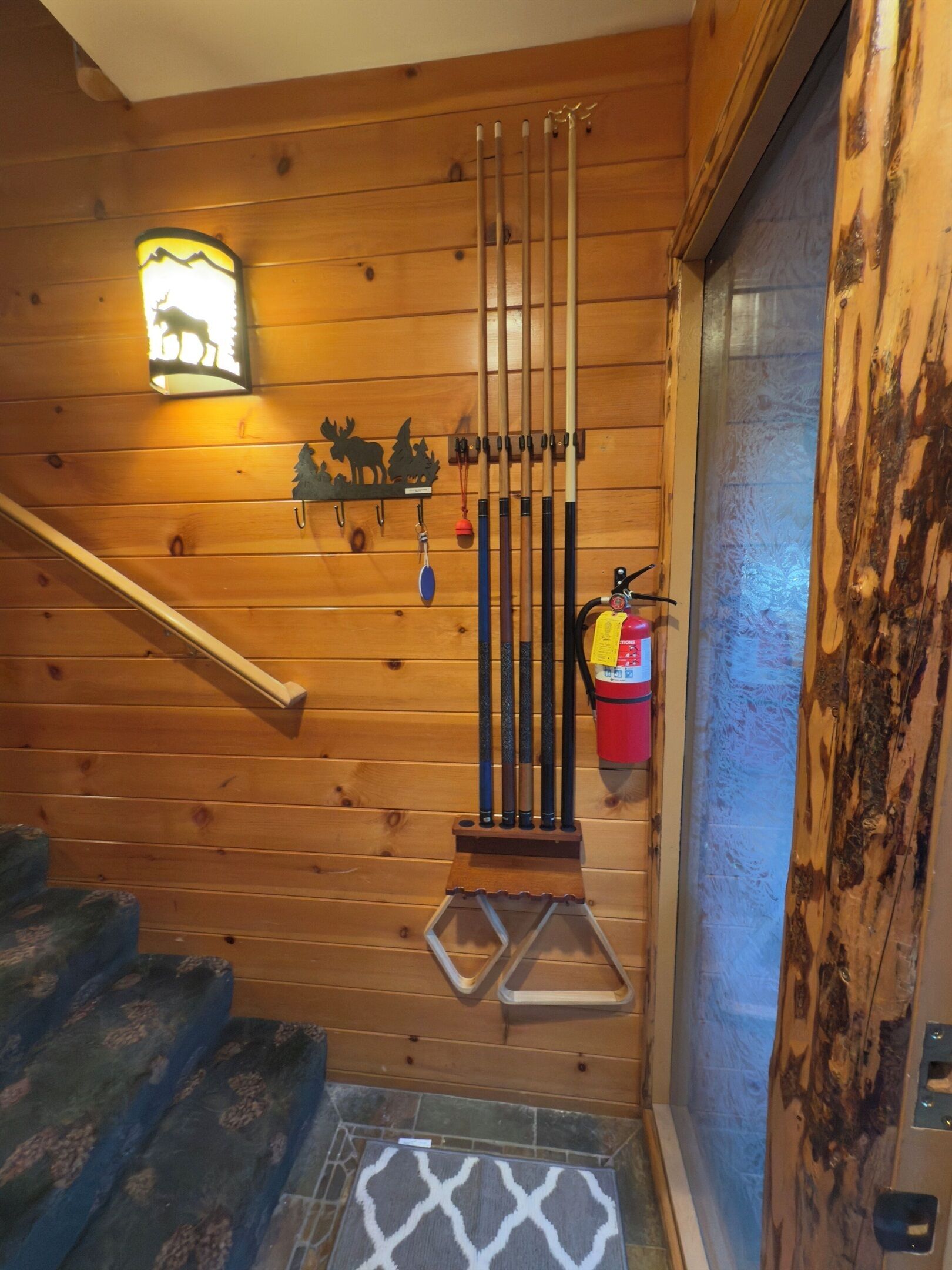 Una escalera de madera con barandilla metálica, un aplique de pared y un extintor.
