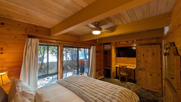 A wooden cabin bedroom with a bed, a desk, and a large window.