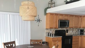 Un'area pranzo con un tavolo rotondo in legno e sedie, un lampadario a sospensione e una cucina con pensili e elettrodomestici in legno.