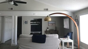 Un soggiorno con un divano bianco, una ventola a soffitto, un tavolo con una lampada e vista sulla cucina.