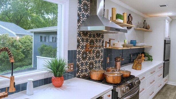 Una cocina moderna con un ventanal grande, armarios blancos, ollas de cobre y una campana extractora de acero inoxidable.