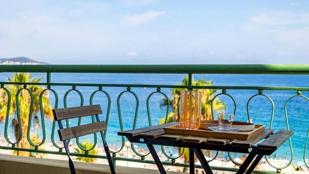 A balcony with a table set for two, overlooking a beach with palm trees and the sea.