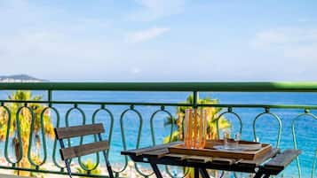 A balcony with a table set for two, overlooking a beach with palm trees and the sea.
