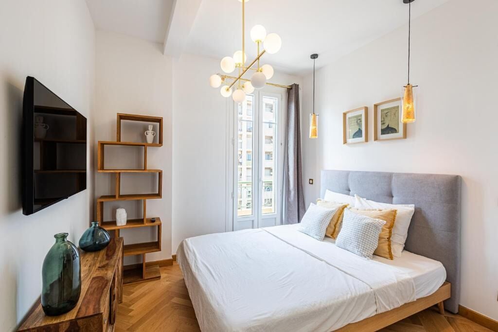 A modern bedroom with a large bed, wooden shelves, a TV, and a chandelier.