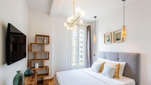 A modern bedroom with a large bed, wooden shelves, a TV, and a chandelier.