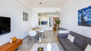 A modern living room with a flat-screen TV, a dining area with a table set for four, and a gray sofa.