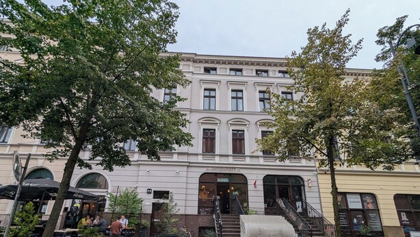 A building with a classic architectural style, featuring a central entrance with a staircase leading to the ground floor.