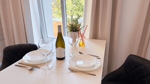 A dining table set with white plates, wine glasses, and cutlery, a bottle of wine, and a small potted plant with red straws.