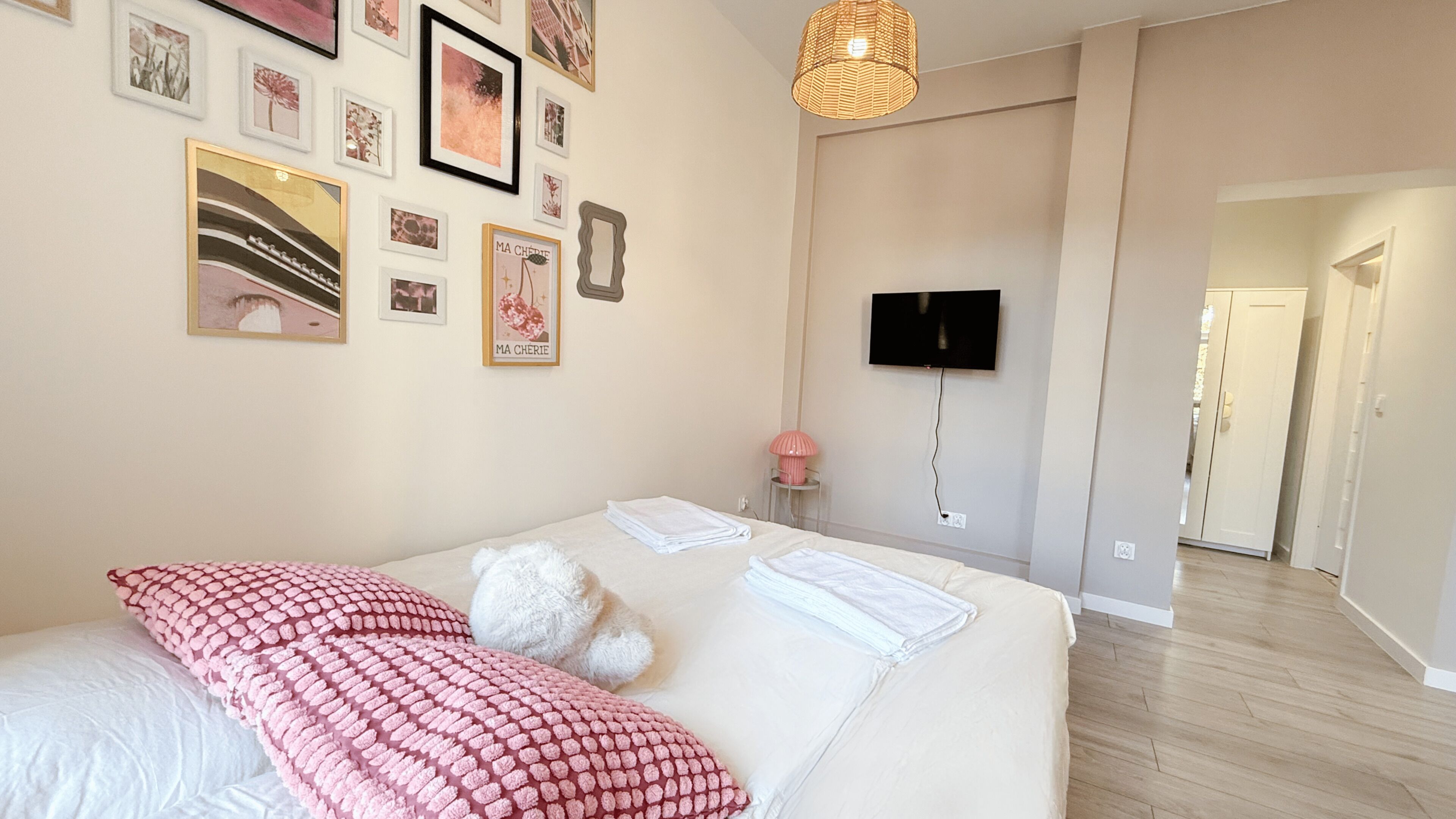 Ein Schlafzimmer mit Bett, Kissen, einem flachbildfernseher an der Wand und einem Flur, der in einen anderen Raum führt.