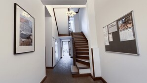 A hallway with a staircase, framed pictures on the walls, and a bulletin board.