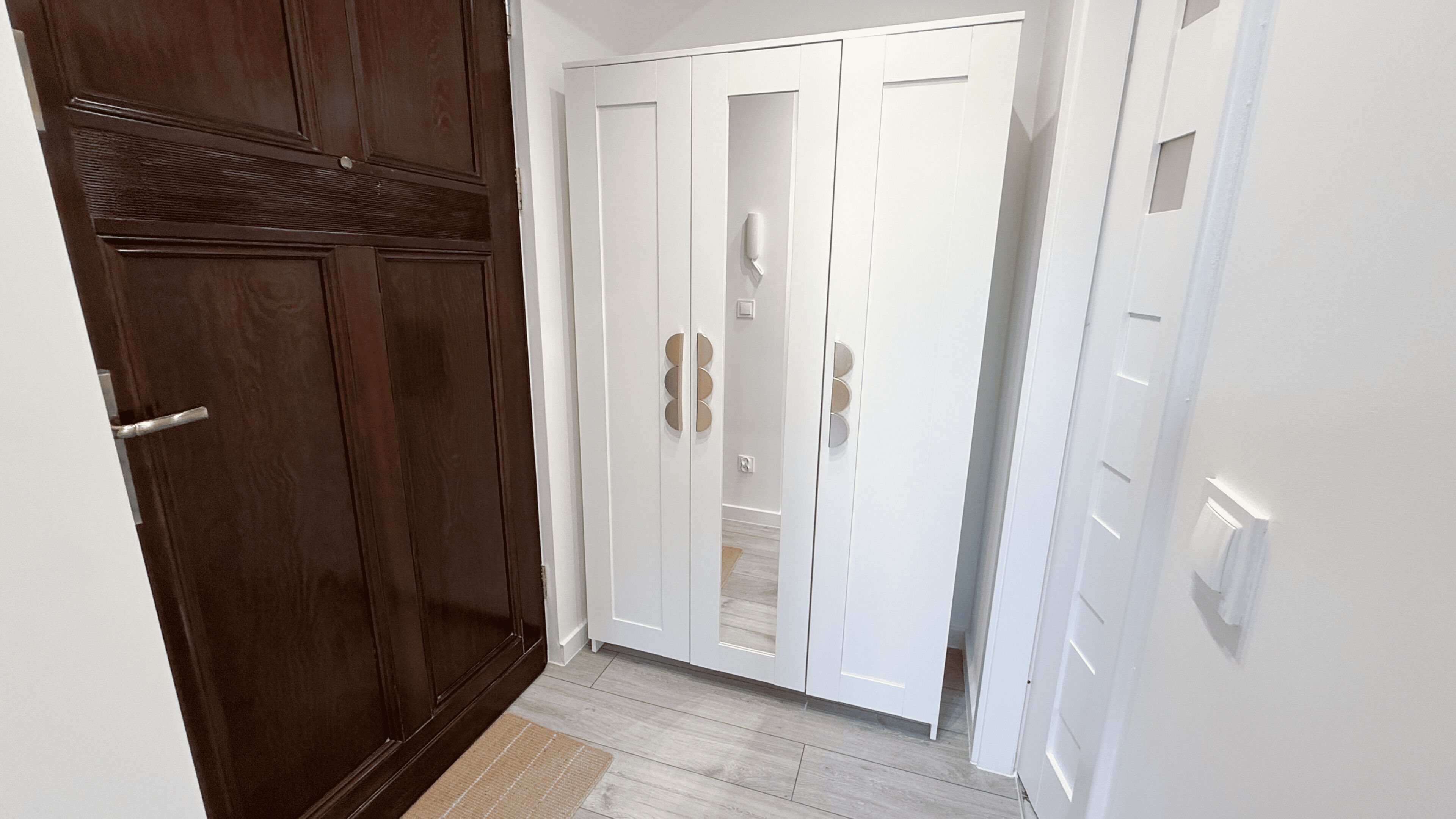 A hallway with a wooden door on the left, a white door with circular handles in the center, and a white door on the right.