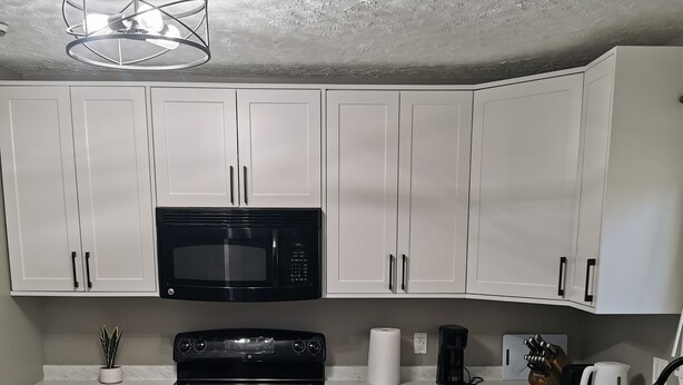 A kitchen with white cabinets, a black microwave, a stove, and a sink. - The Grand Estate- 4 Bedroom  (Moncton)