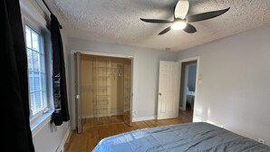 A bedroom with a bed, a ceiling fan, a walk-in closet, and a door leading to another room. - The Grand Estate- 4 Bedroom  (Moncton)
