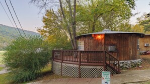 A rustic wooden cabin with a deck, surrounded by trees and a mountain backdrop. - Adventurer Yurt - Landing Zone, Studio. Full Bathroom. Kitchenette. Updated. (Wildwood)