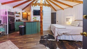 A cozy attic bedroom with a wooden ceiling, a bed, a small kitchenette, and a TV mounted on the wall. - Adventurer Yurt - Landing Zone, Studio. Full Bathroom. Kitchenette. Updated. (Wildwood)