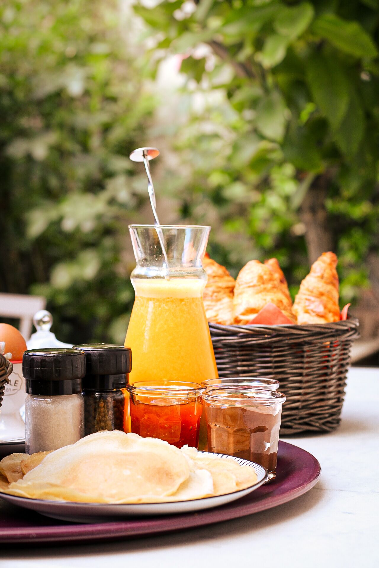 A breakfast setting with a plate of crepes, a glass of orange juice, and a basket of croissants.