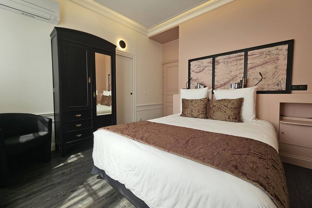 A hotel room with a large bed, a dark wooden wardrobe, a desk, and a wall-mounted artwork.