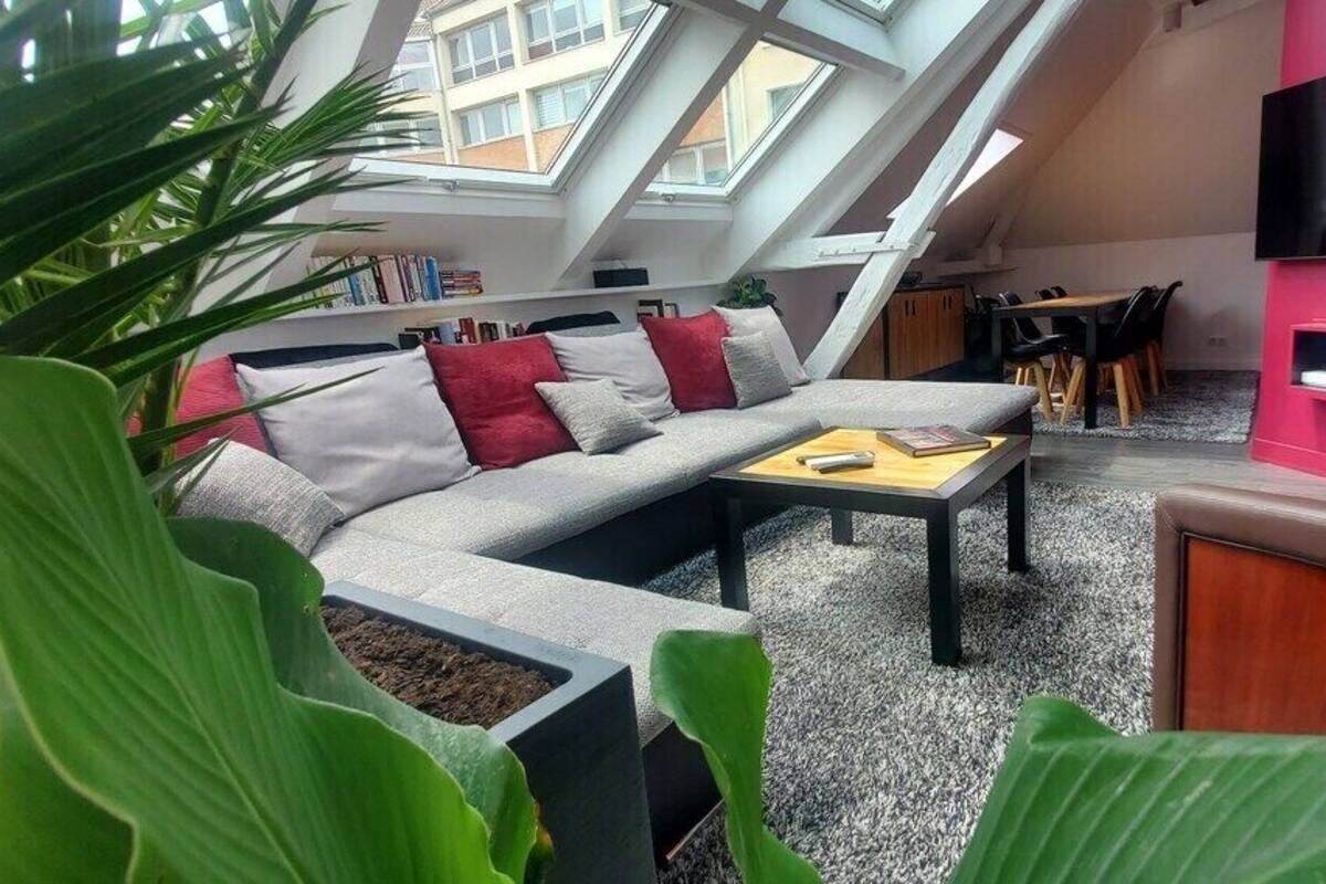 A modern living room with a high ceiling, skylight, and a flat-screen TV mounted on a pink wall.