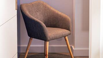 Een moderne fauteuil met houten poten en een gestructureerde stof, geplaatst in een kamer met een effen muur en een deur.