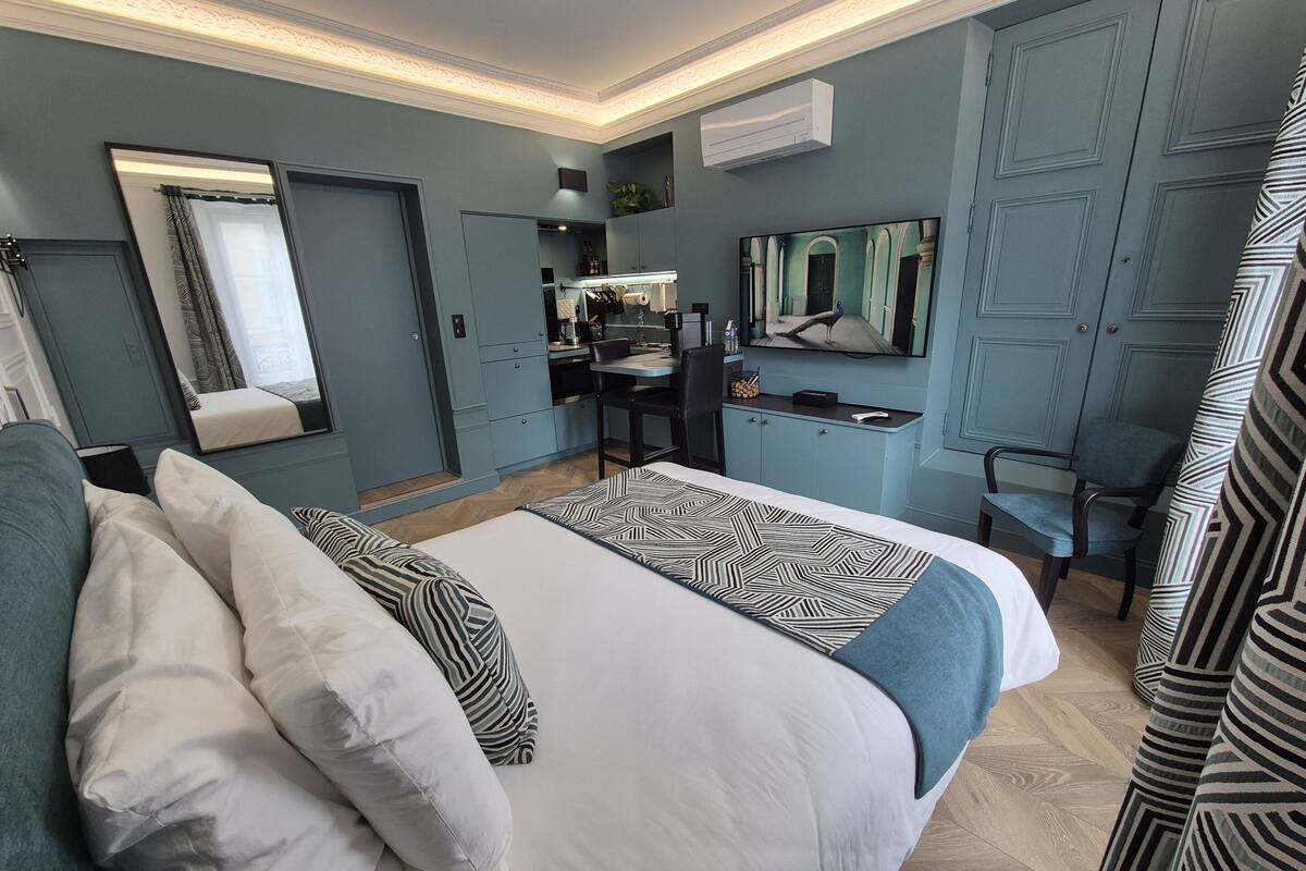 A modern hotel room with a large bed, a desk, a mirror, and a television.
