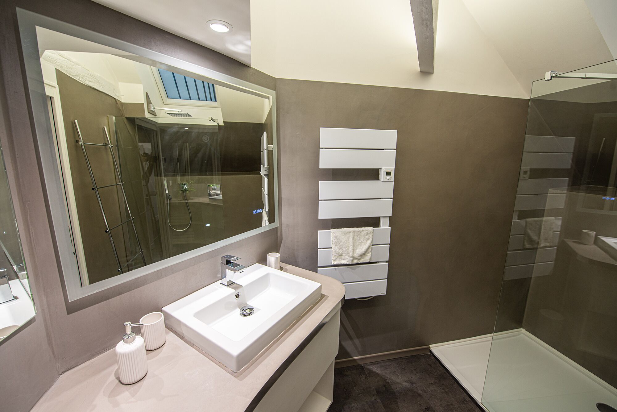 A modern bathroom with a large mirror, a white sink, a glass shower enclosure, and a towel rack.