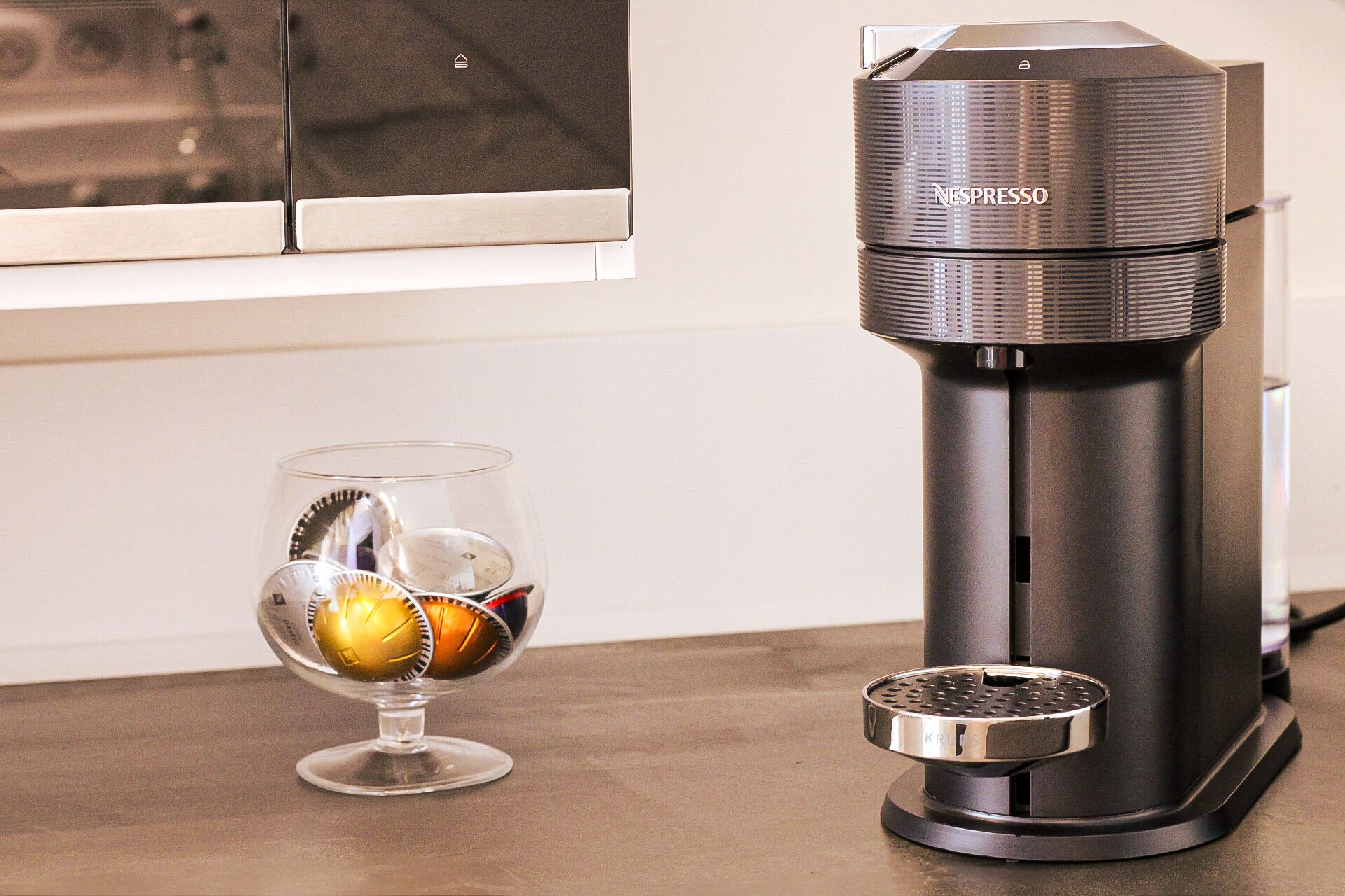 A Nespresso coffee machine next to a glass with a metal cup.