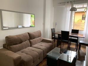Ett vardagsrum med en brun soffa, ett soffbord i glas och en matplats med ett bord och stolar.