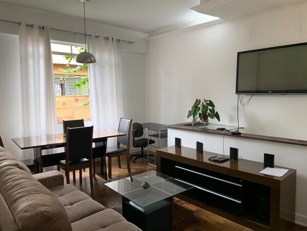 Ett modernt vardagsrum med en soffa, ett matbord, stolar, en tv och en växt.