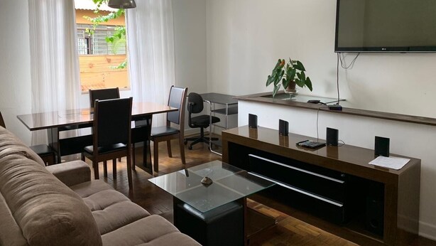 A modern living room with a sofa, dining table, chairs, a TV, and a plant.