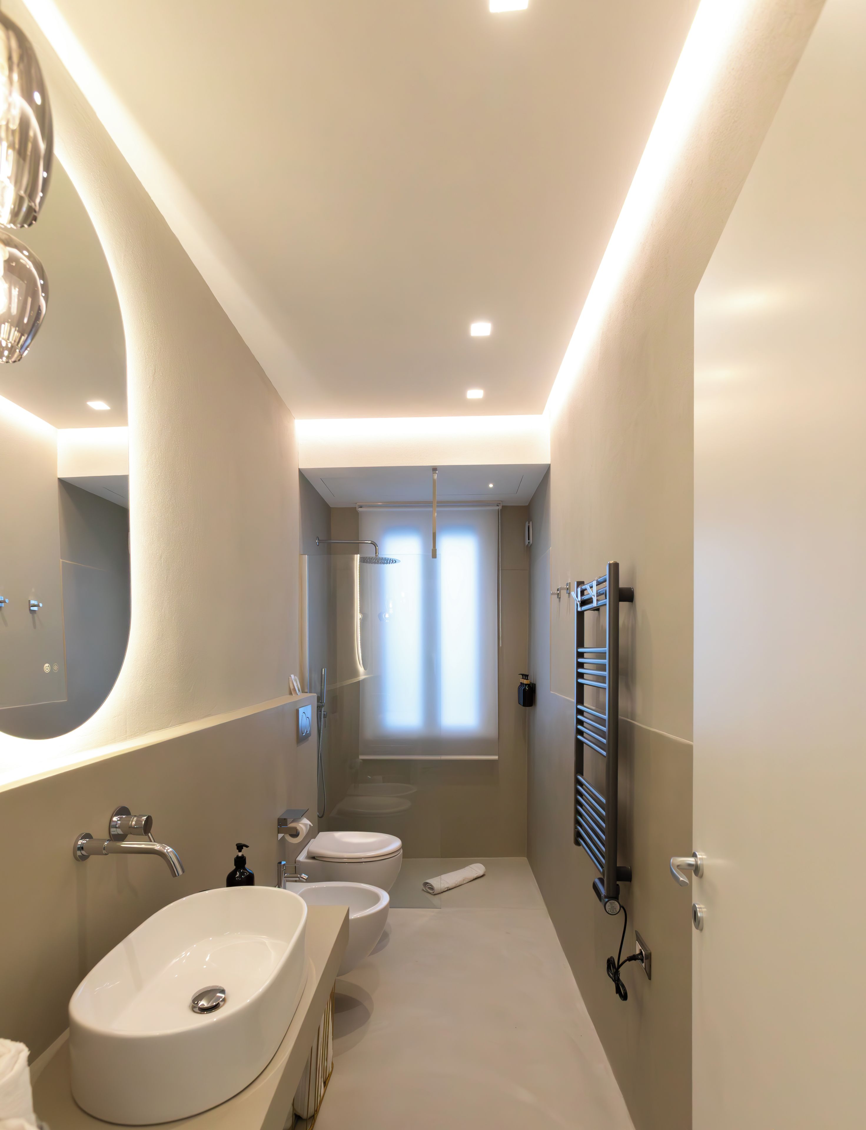 A modern bathroom with a large mirror, two sinks, a towel rack, and a shower area.