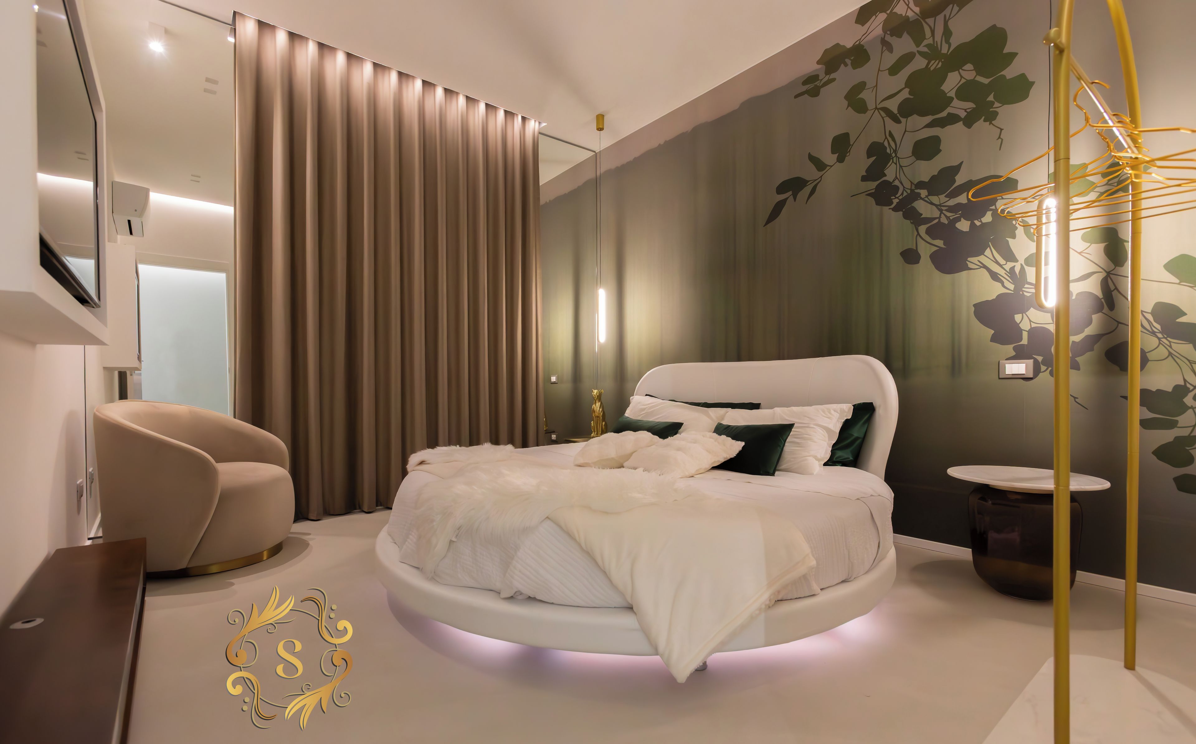 Un dormitorio moderno con cama redonda, sofá, televisor y una planta decorativa.