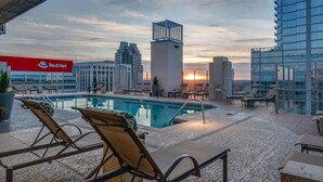 A rooftop pool area with lounge chairs, a Red Hat sign, and modern buildings in the background.