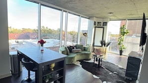 A spacious living area with a large window, a green sofa, a dining table, and a black leather rug.