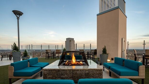 A rooftop terrace with a fire pit, outdoor seating, and a view of the city skyline.