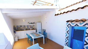 A compact outdoor dining area with a table and chairs, a kitchen in the background, and a patterned wall. - Your beach house in Sicily, Casa Sciàpò (Terrasini)